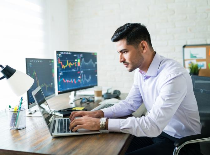 Broker trading through laptop at desk while working from home