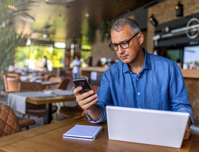 Businessman using smartphone and laptop computer in cafe.